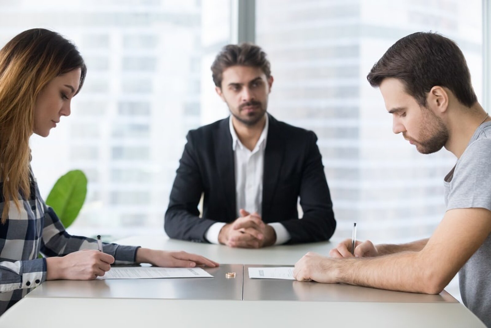 A couple signs paperwork with a mediator seated between them at a table